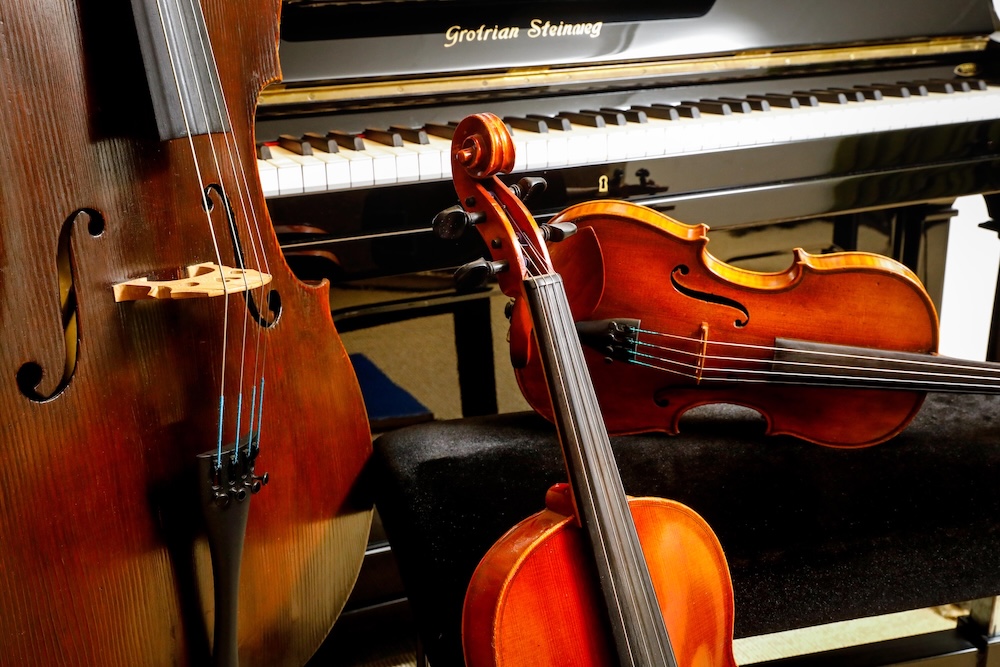 Foto met een aantal strijkinstrument die tegen een piano leunen