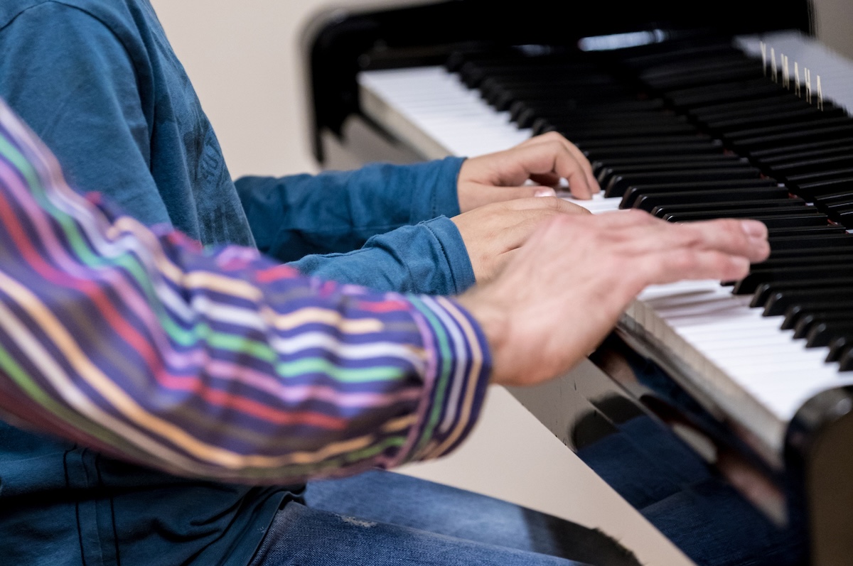 Foto van twee paar handen op een piano toetsenbord, van een volwassene en een kind.